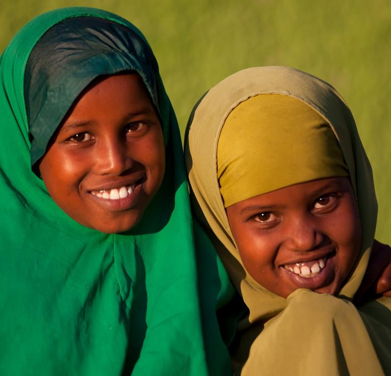 Two girls with headscarves on smile for the camera.