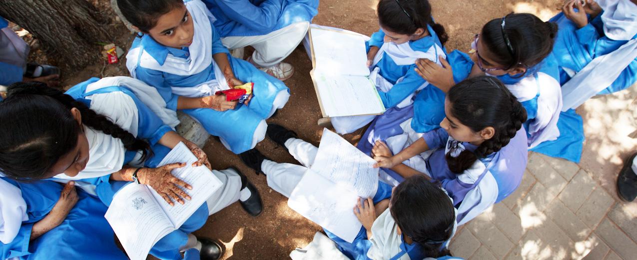 Schoolgirls at an Aahung partner school reading in the shade of a tree. © Aahung
